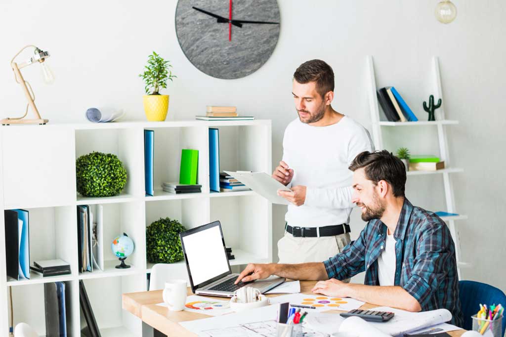 Two men are working on a laptop in an office.