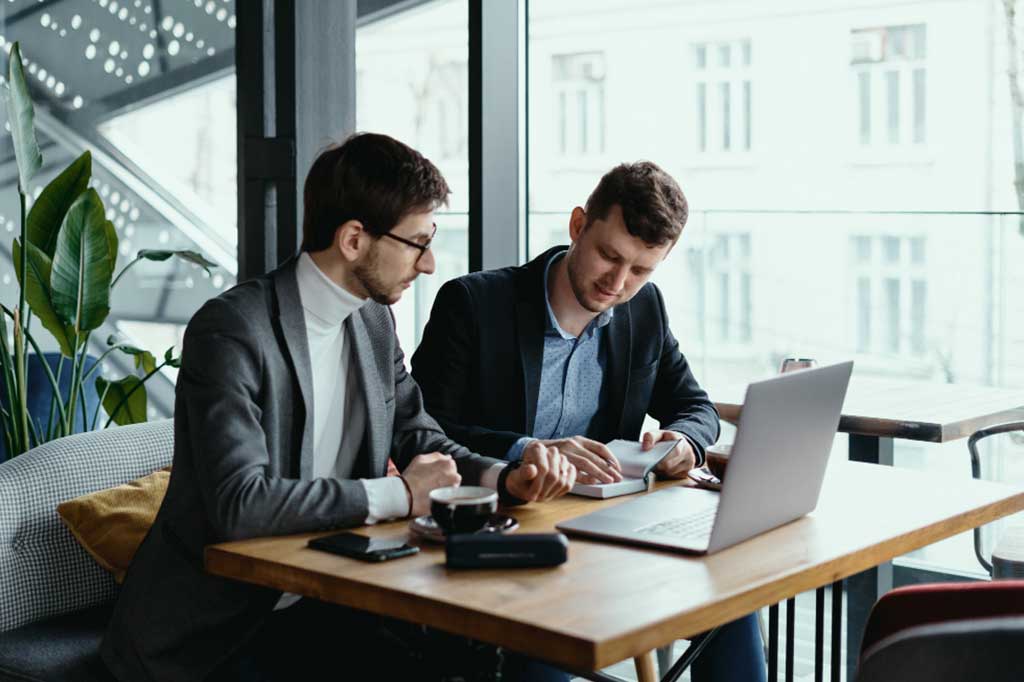 Two men sitting at a table looking at a laptop.