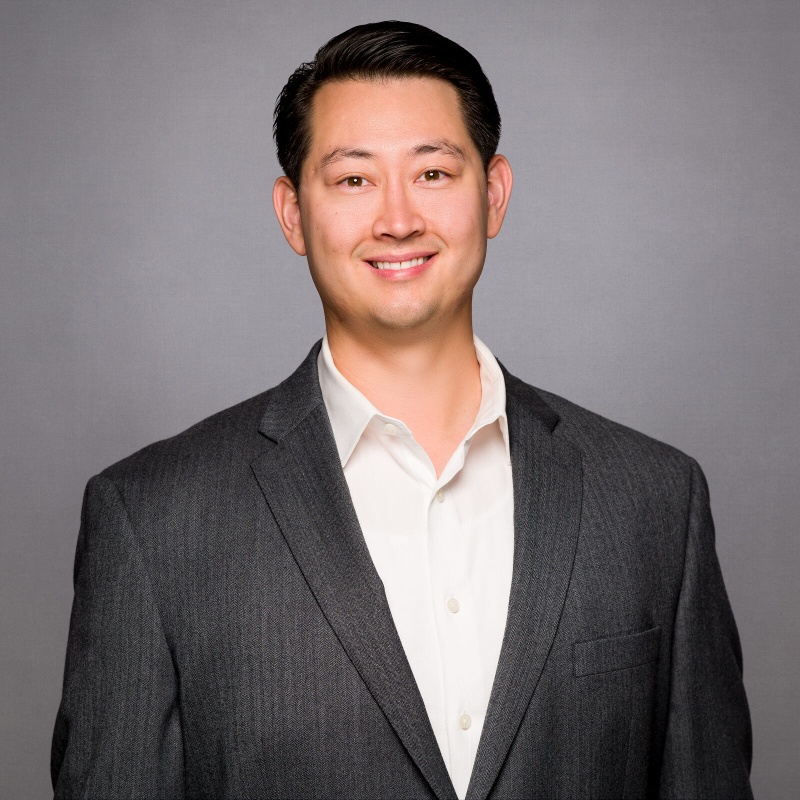 A man in a suit and tie standing up against a gray background.